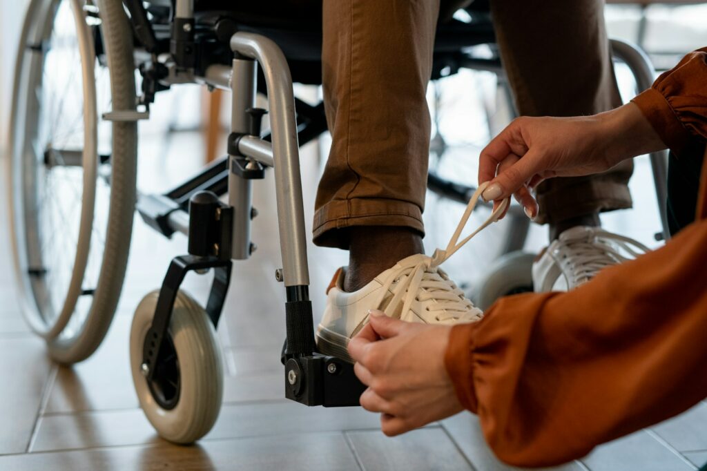 Hands of young female carer tying shoelace on footwear of man with disability